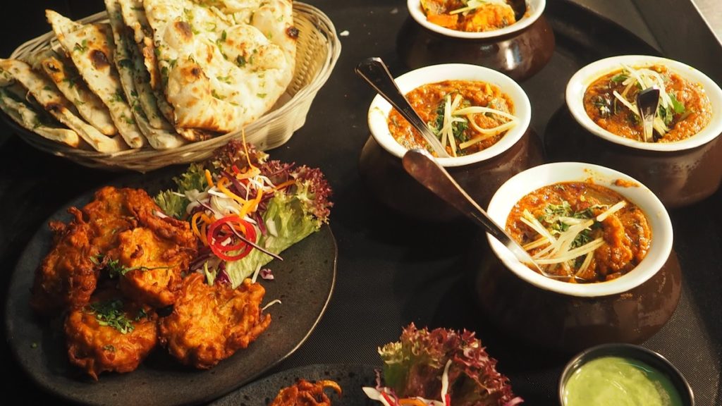 A restaurant spread of food showing a basket of naan, a plate of fritters and bowls of curry.