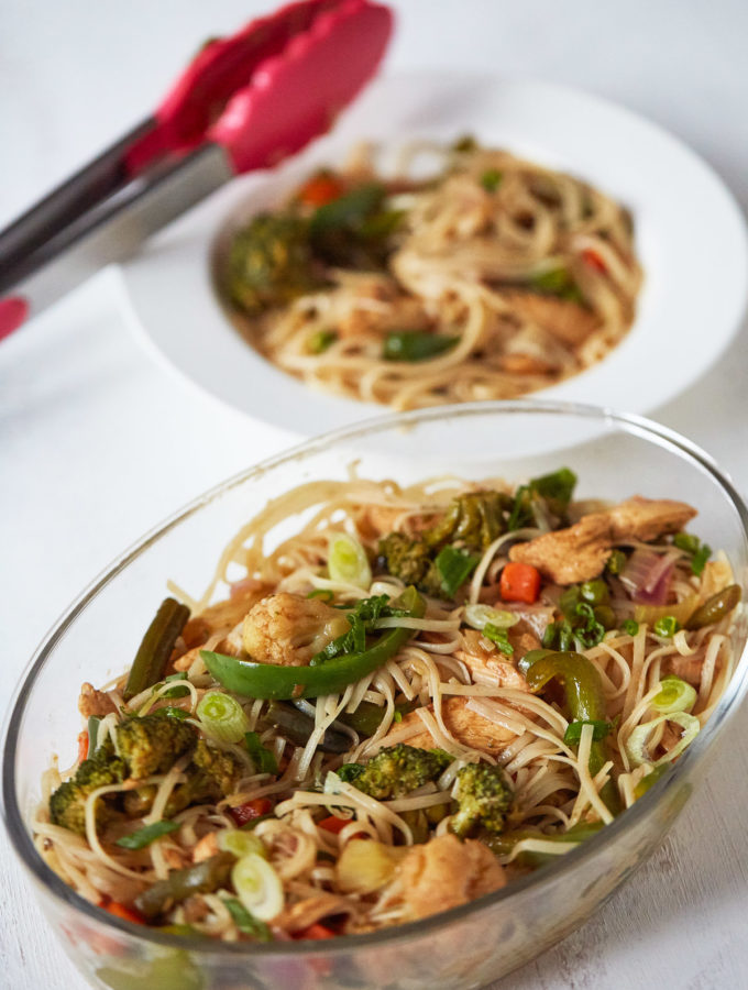 Chicken Stir Fry with Noodles in an oblong glass dish with plated stir fry with noodles in the background