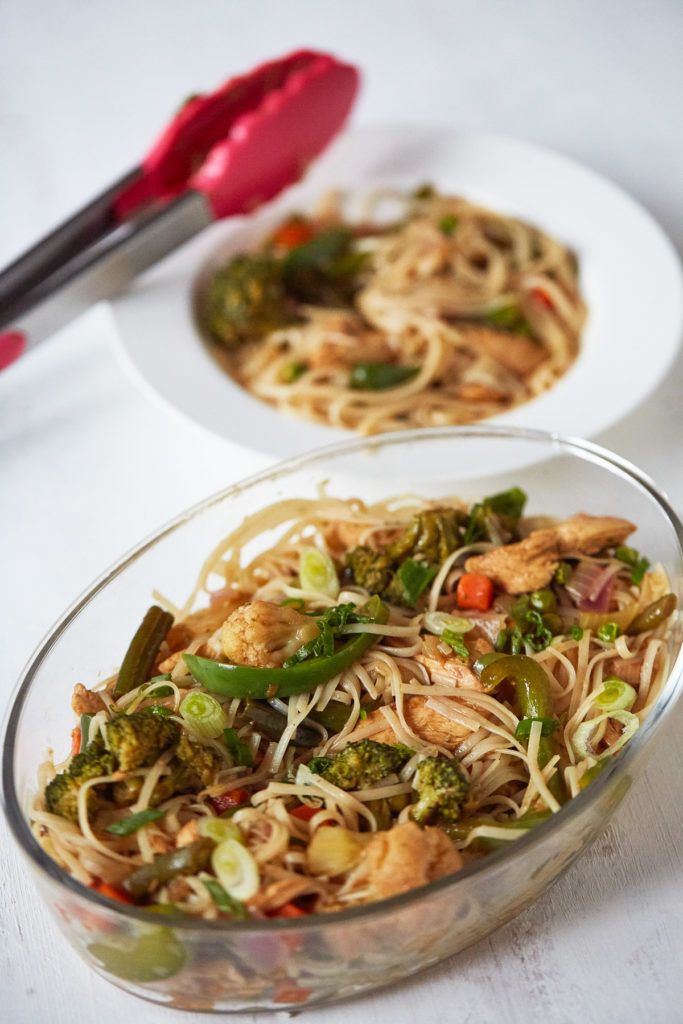 Chicken Stir Fry with Noodles in an oblong glass dish with plated stir fry with noodles in the background