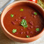 Rajma Masala or Lal Lobia (Red Kidney Bean Curry) in a clay bowl, garnished with coriander, shot at a 45 degree angle with a knife and a tomato in the background.