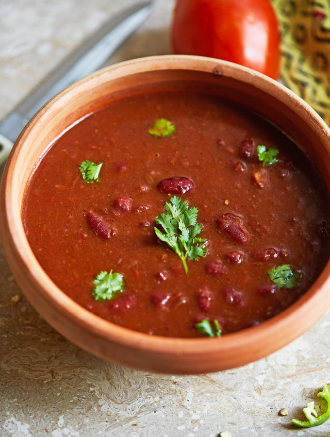 Rajma Masala or Lal Lobia (Red Kidney Bean Curry) in a clay bowl, garnished with coriander, shot at a 45 degree angle with a knife and a tomato in the background.